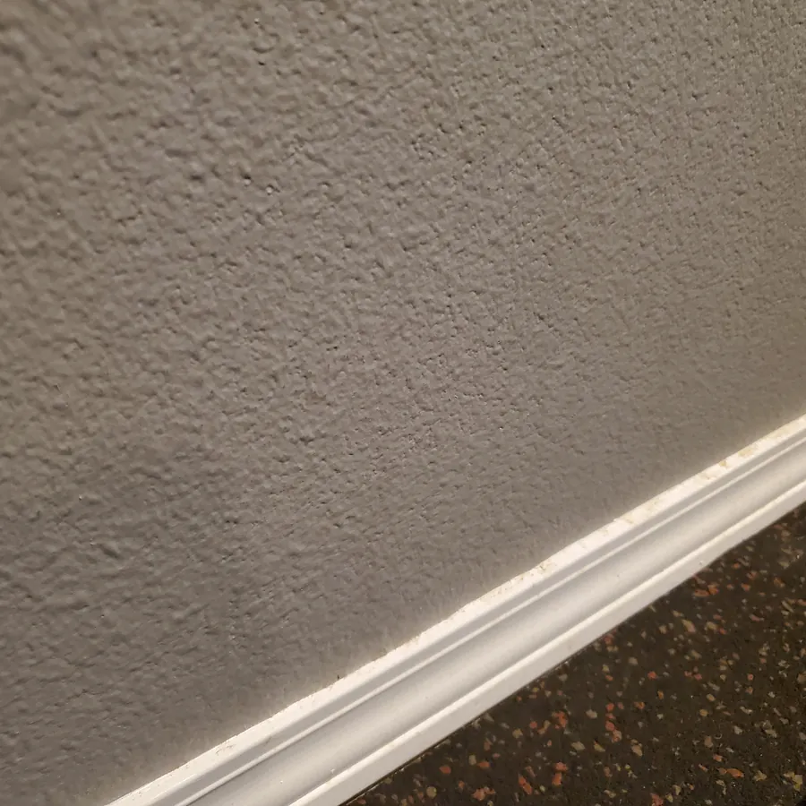 The same wall and baseboard before cleaning, with scuffs and dust