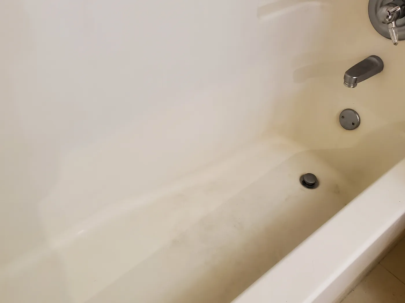The same bathtub before cleaning, dull with soap scum and grime