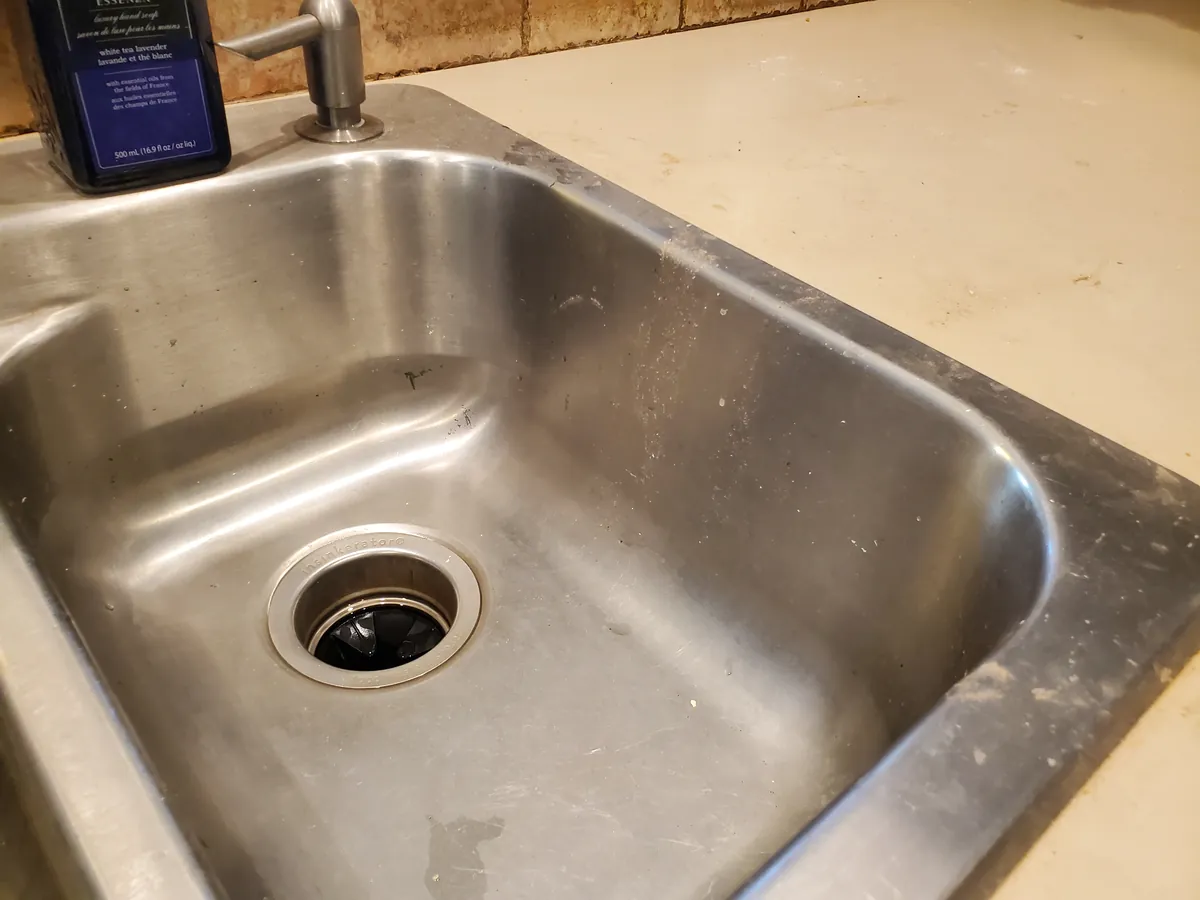The same kitchen sink before cleaning, with water spots and residue