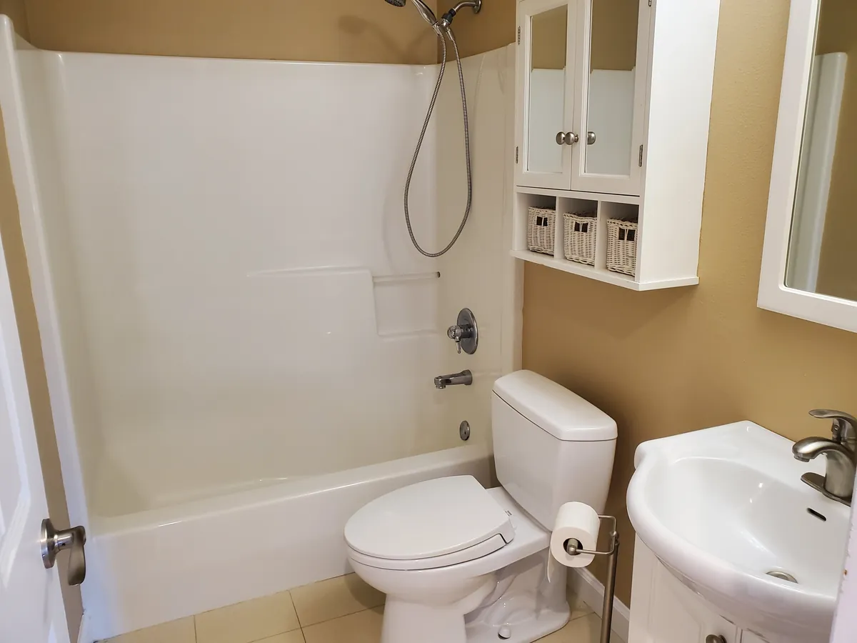A full bathroom after a deep clean: gleaming tub surround, toilet, pedestal sink, and mirror