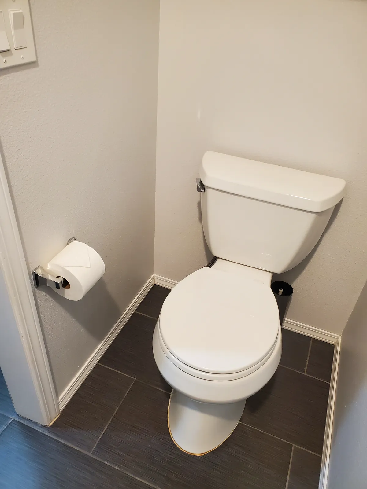 Half bathroom after a clean, with a white toilet and dark tile floor