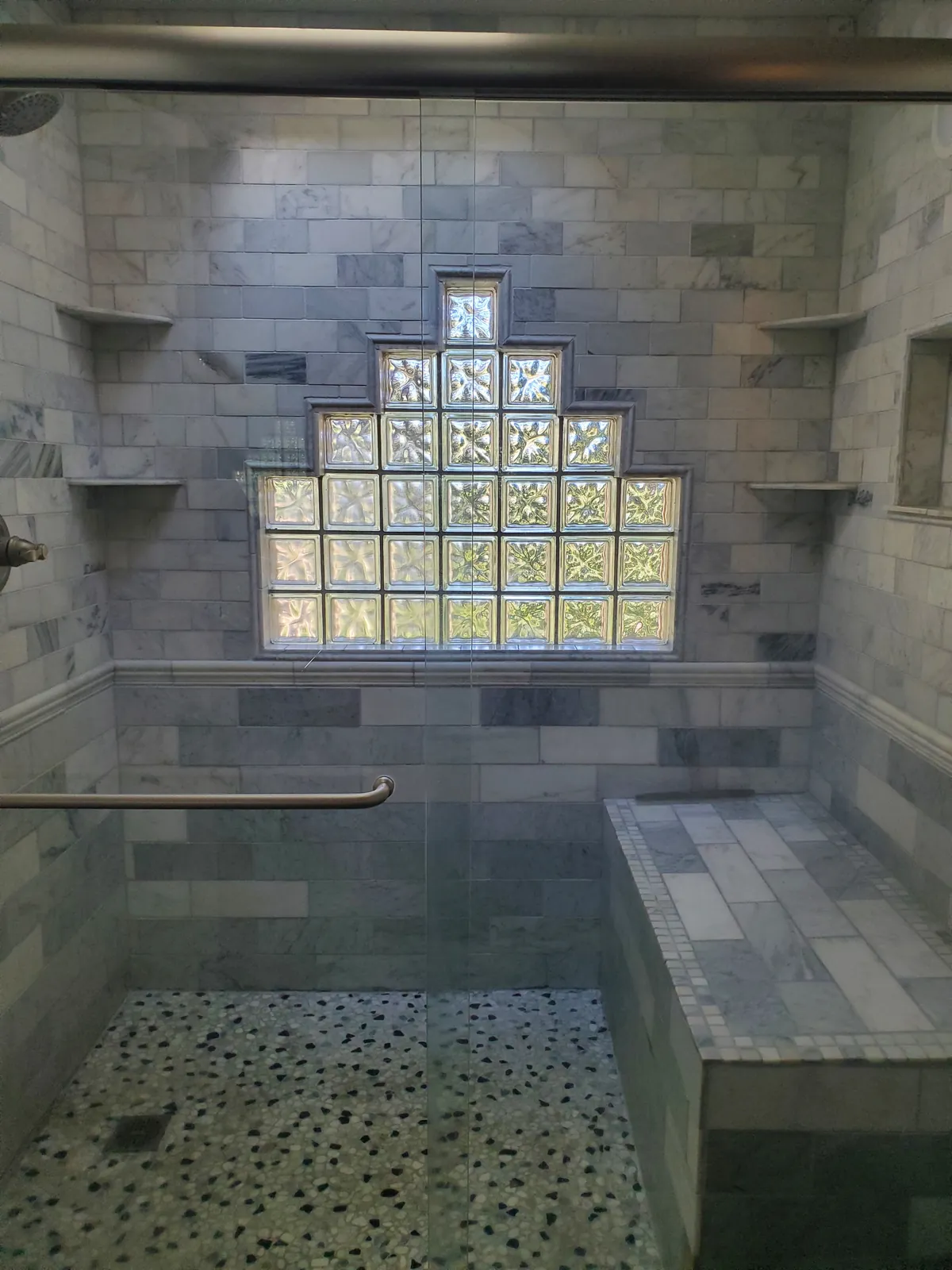 Tiled walk-in shower after a clean, with a glass-block window and pebble floor