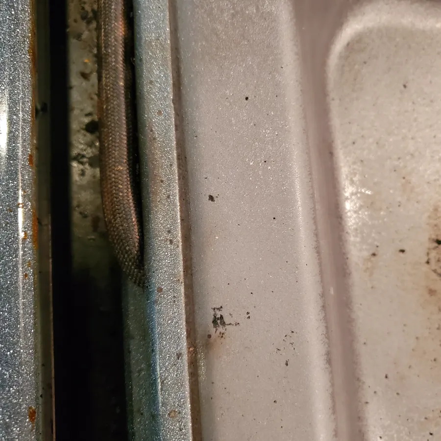 The same oven door edge before cleaning, with crumbs and baked-on grime